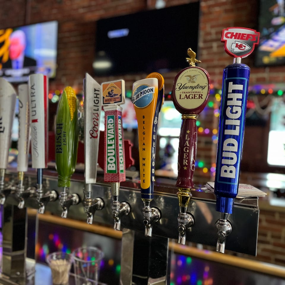 Close-up of beer taps at Emerson Biggins sports bar, featuring various brands and a Chiefs tap.