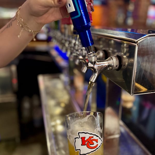 A hand pours beer from a tap into a glass with a Kansas City Chiefs logo.