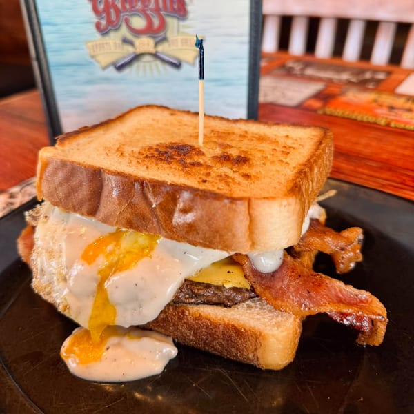 A breakfast sandwich with bacon, egg, and cheese on toast, with a runny yolk and sauce.