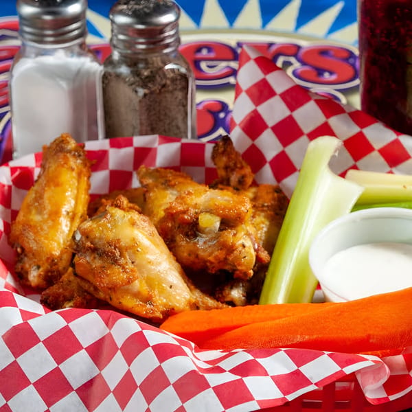 Emerson Biggins' crispy chicken wings in a red basket with celery, carrots, and ranch dressing.