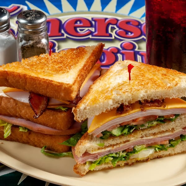 Two toasted club sandwiches with bacon, cheese, and deli meat, with salt and pepper shakers.