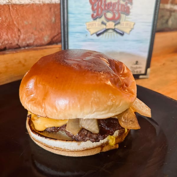A juicy Emerson Biggins cheeseburger with caramelized onions on a black plate, with a menu in the background.