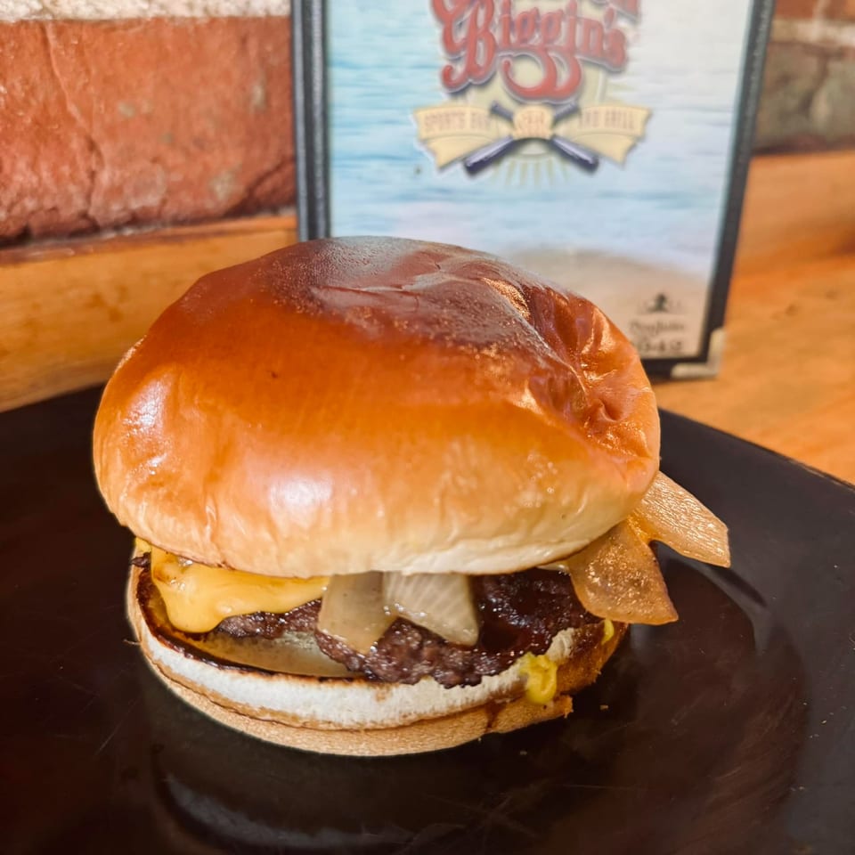 A juicy Emerson Biggins cheeseburger with caramelized onions on a black plate, with a menu in the background.