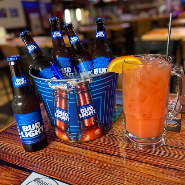 A bucket of Bud Light beers and a tall glass of orange cocktail with an orange slice.