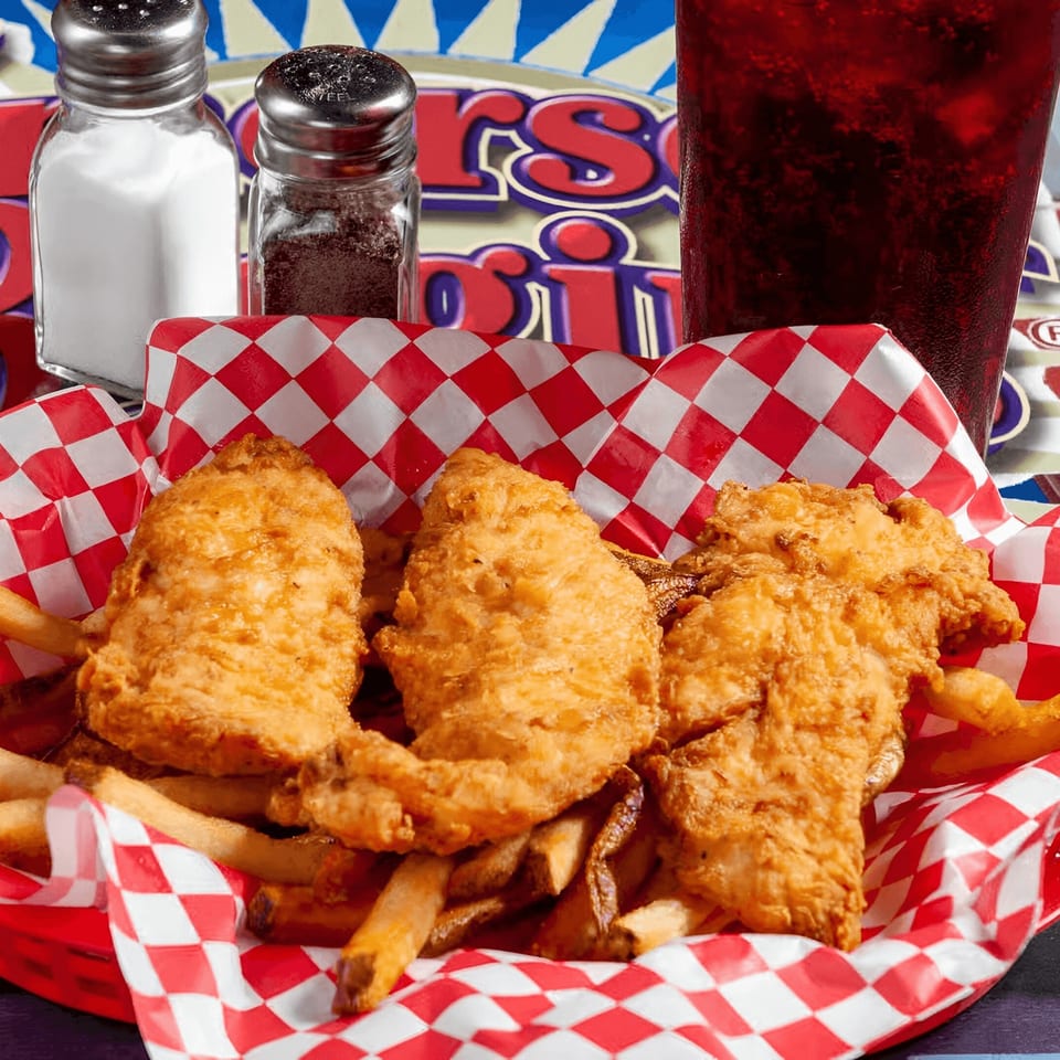 Crispy chicken tenders and fries in a red and white checkered basket, with a drink and shakers.