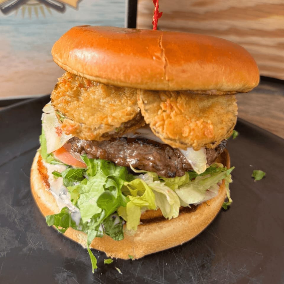 A large burger with fried pickles, lettuce, tomato, and sauce on a dark plate.