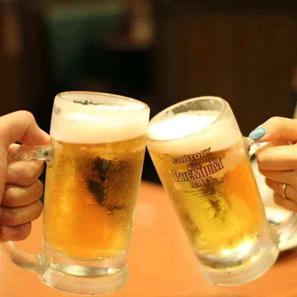 Two hands clinking frosty mugs of beer, one with "Suntory The Premium Malt's" logo.
