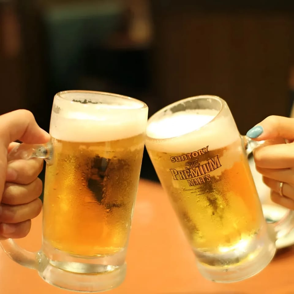 Two hands clinking frosty mugs of beer, one with "Suntory The Premium Malt's" logo.