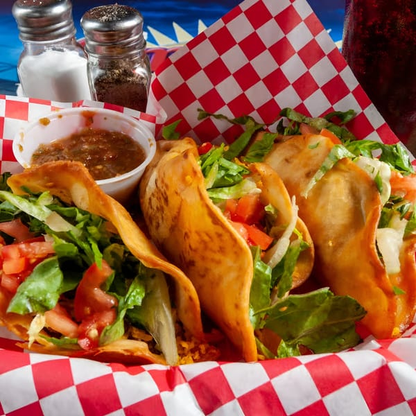 Three crispy tacos filled with lettuce, tomatoes, and meat, served with salsa and salt and pepper shakers.