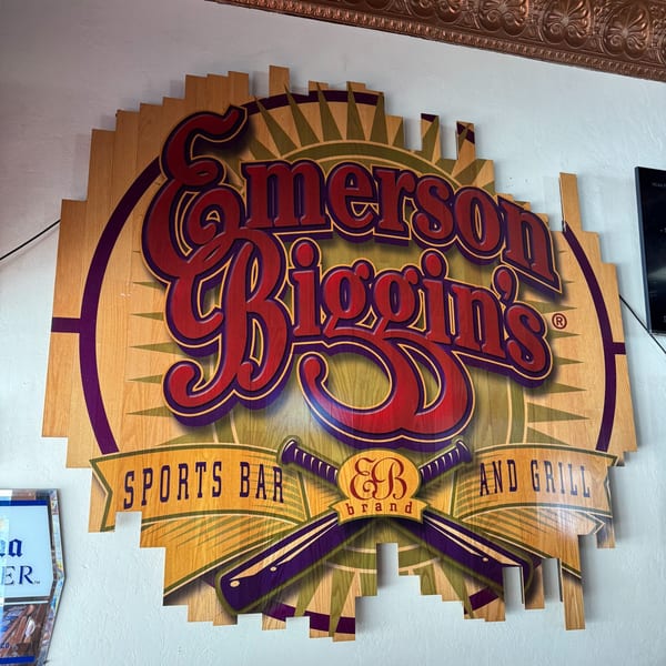 A wooden sign for Emerson Biggins Sports Bar and Grill, featuring baseball bats and a sunburst design.