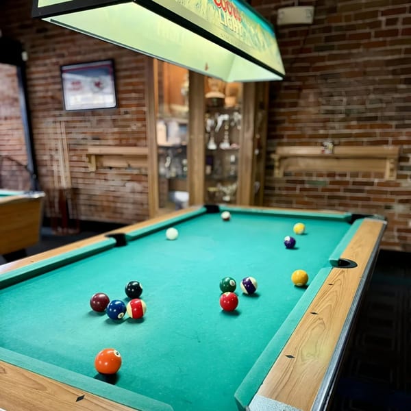 A pool table with colorful billiard balls scattered across its green felt surface at Emerson Biggins.